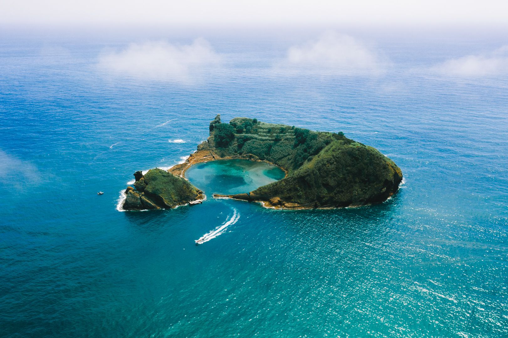 A ringed green islet from above, boat passing, Azores.