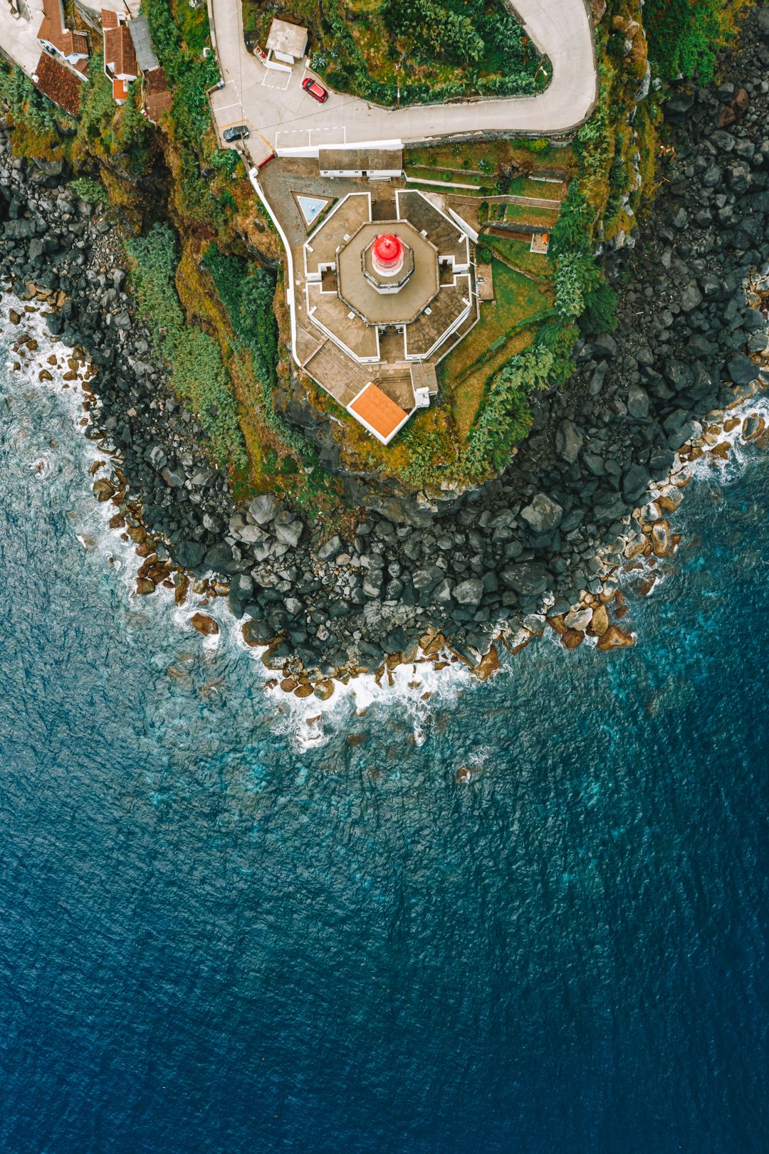 A lighthouse on the point from directly above, waves on the rocks, Azores.