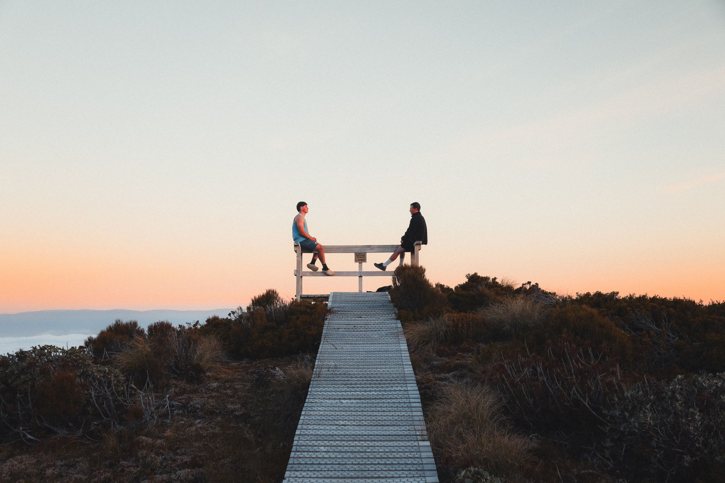 Two brothers sitting on a lookout rail above the clouds at sunset, Humpridge Track.