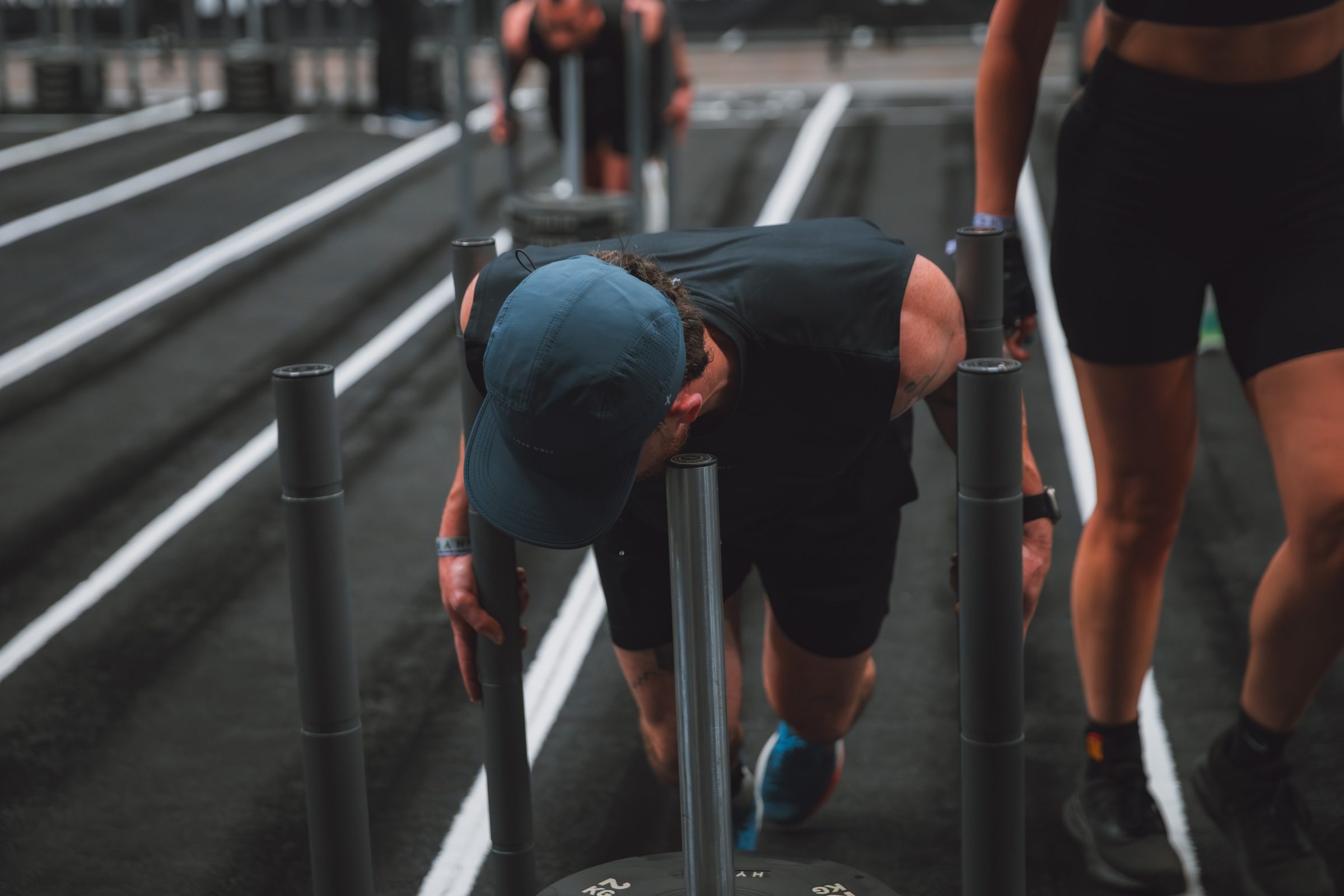 Head down over the sled, lanes running away behind, HYROX race floor.