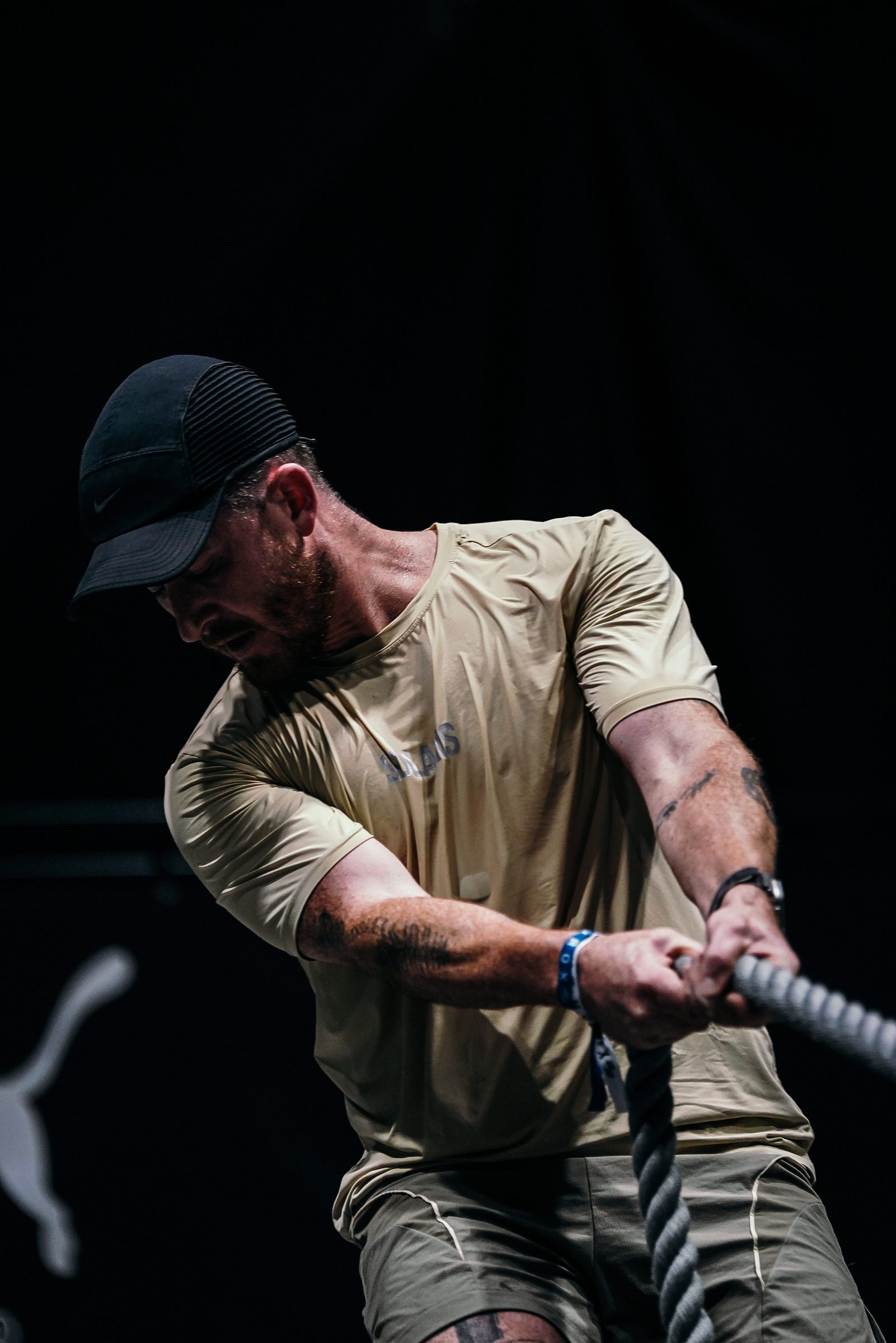 Hauling the rope against a black wall, hard side light on a soaked shirt.