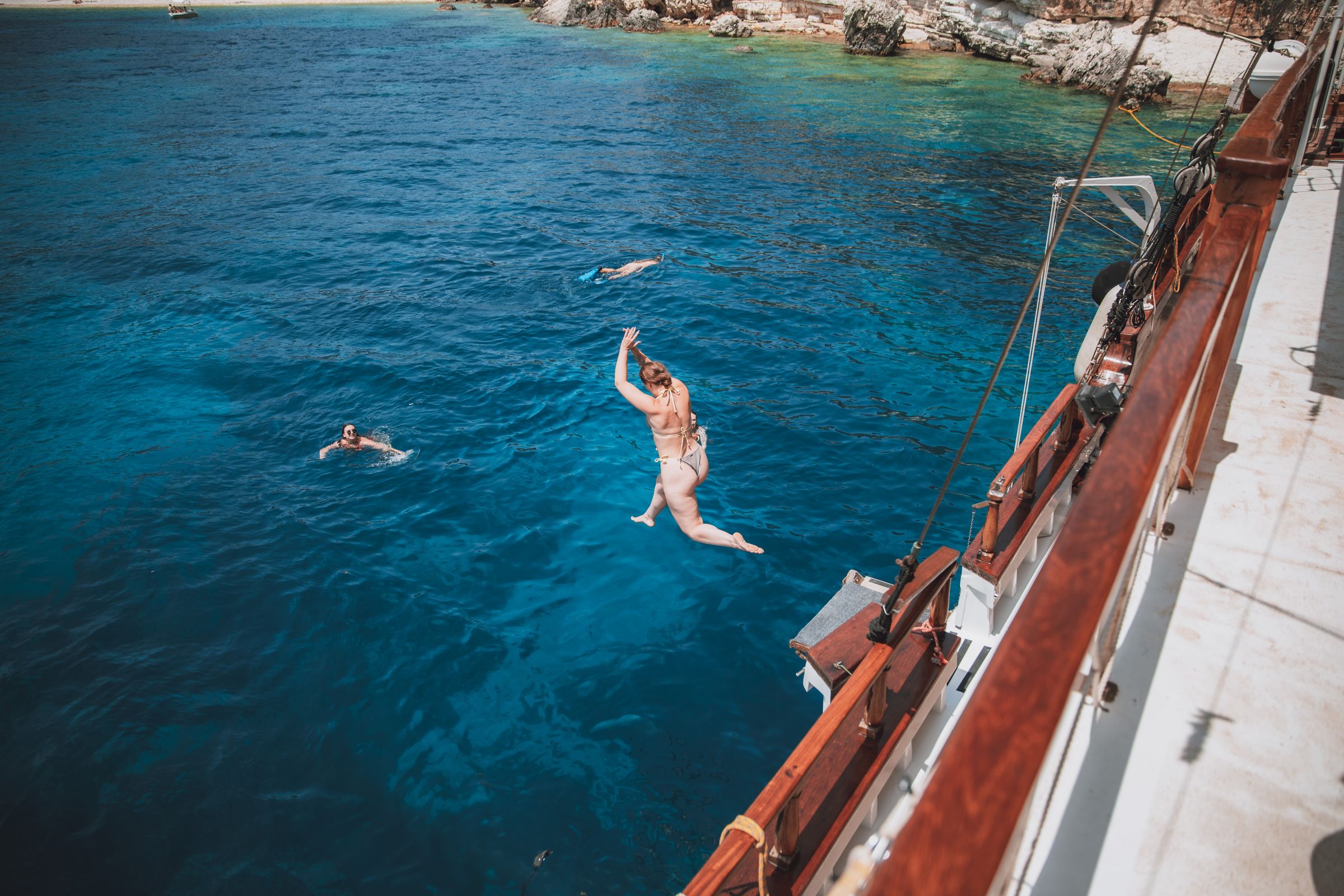 Mid-air leap from the deck of a sailing boat into deep blue water.