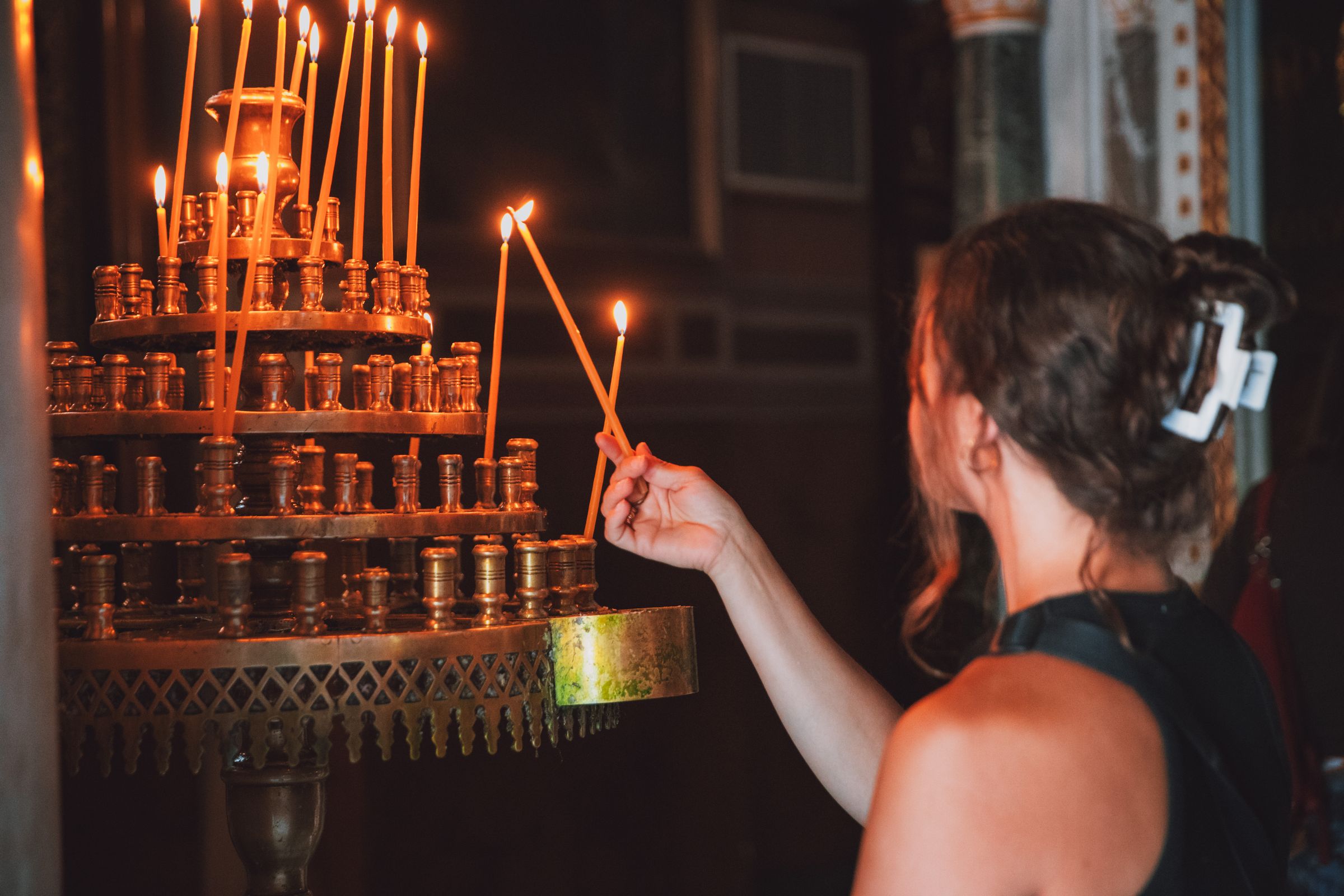 Lighting candles inside a dim Athens chapel, warm flame light.