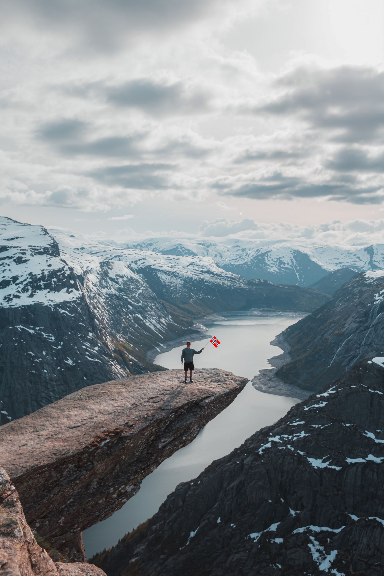 Standing on Trolltunga with a flag, the fjord far below, Norway.