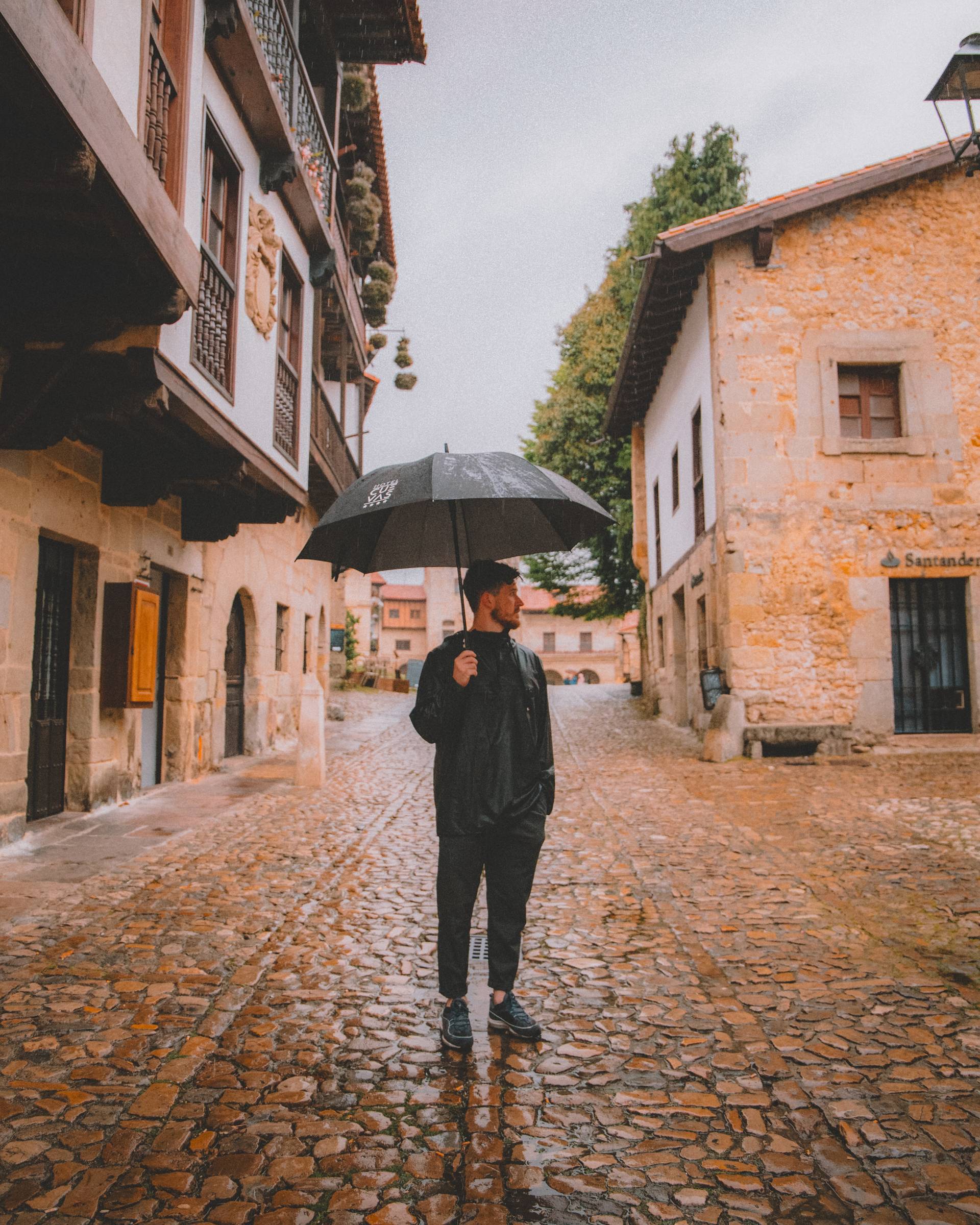 Rain on the cobbles of Santillana del Mar, one figure under a black umbrella.